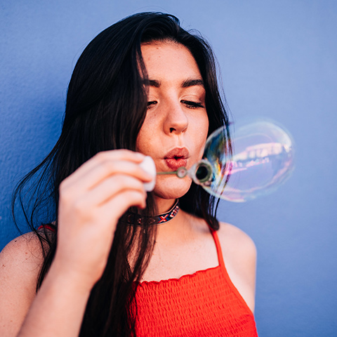 Girl in a red dress with long black hair blowing bubbles
