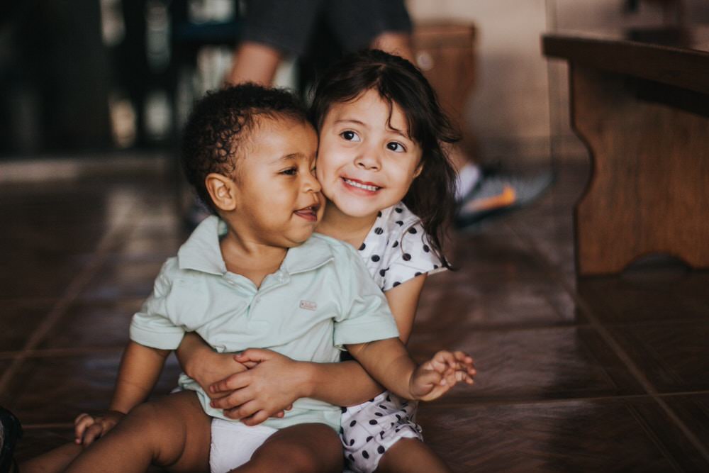 Toddler hugging laughing baby and smiling at camera