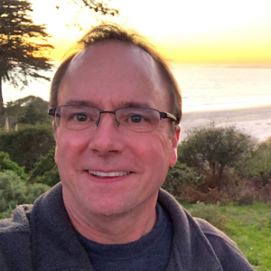 Image of a man smiling with a beach sunset in the background